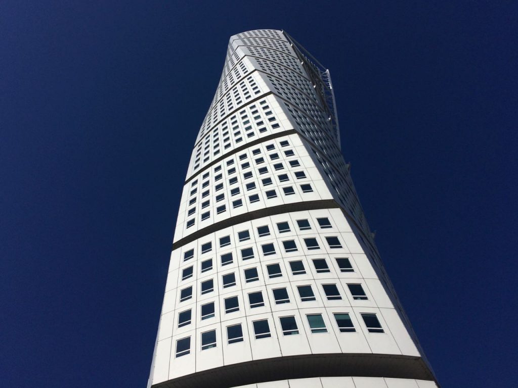 Image of the Turning Torso Tower, in Malmö, Sweden. The twisting helical structure is photographed from below and gleams white against a dark blue sky. This photo is used to advertise a conceptual design training course for structural engineers