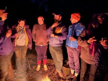 Four workshop participants stand around a fire in the woods