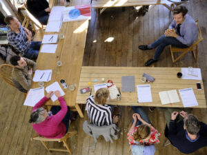 View from above of a group of participants sitting in a horse-shoe with Oliver Broadbent facilitating in the middle