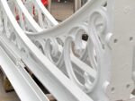 Close-up of ornate white-painted cast iron sections with curved scrollwork patterns, stacked on site.