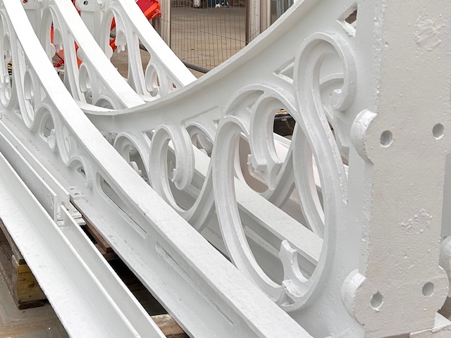 Close-up of ornate white-painted cast iron sections with curved scrollwork patterns, stacked on site.